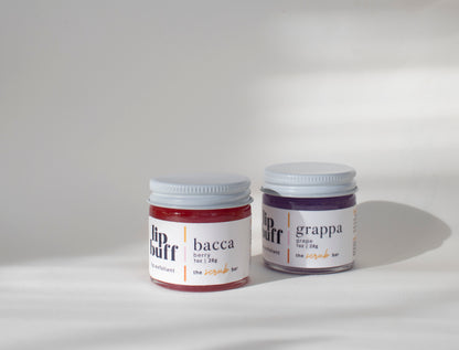 "Two jars of The Scrub Bar's handmade exfoliating lip scrubs, one in berry and the other in grape scents. The lip scrubs are designed to exfoliate lips, helping to maintain soft, hydrated lips. Ideal for regular lip care with natural, effective ingredients.