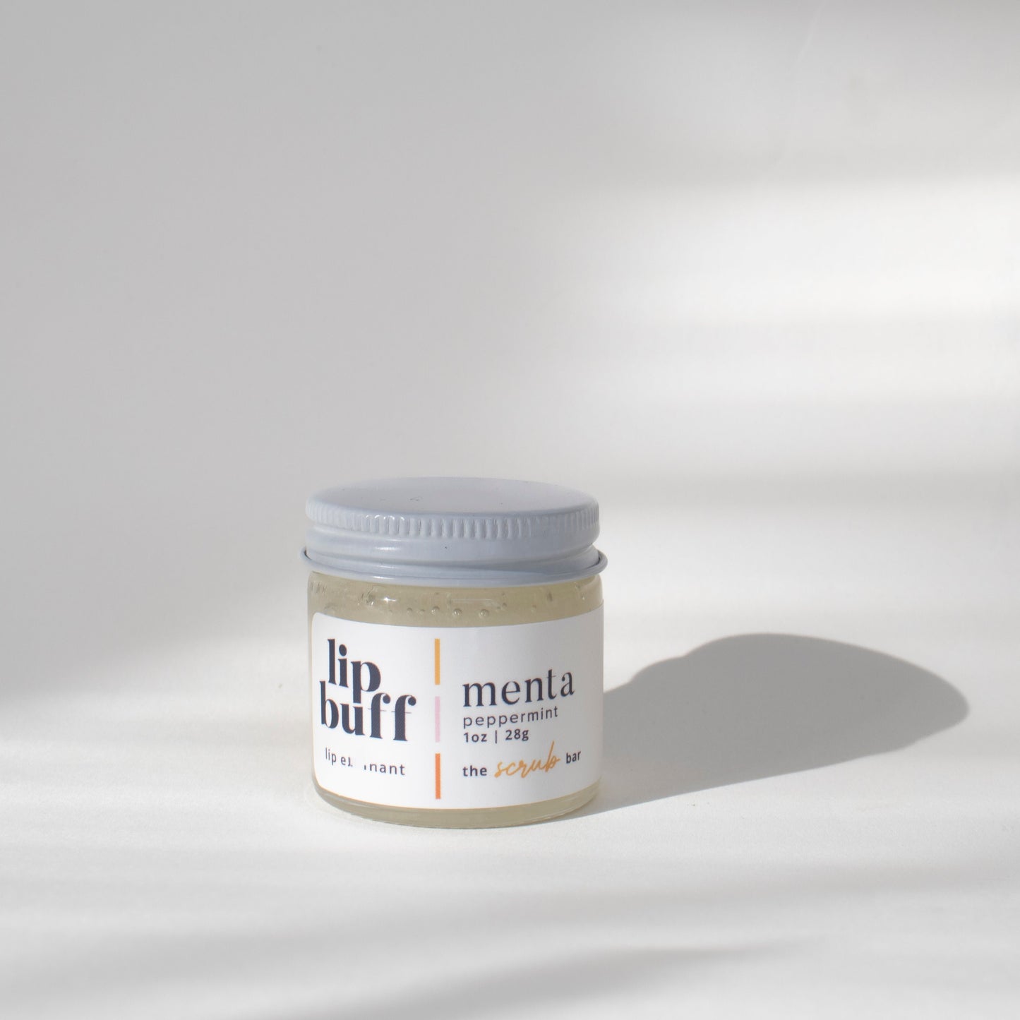 Menta Lip Buff- Close-up of The Scrub Bar's handmade  exfoliating lip scrub in a clear jar with a white lid. The scrub is peppermint-scented and is designed to exfoliate lips, revealing smoother, moisturized skin. Perfect for prepping pouted lips for lip care routines."