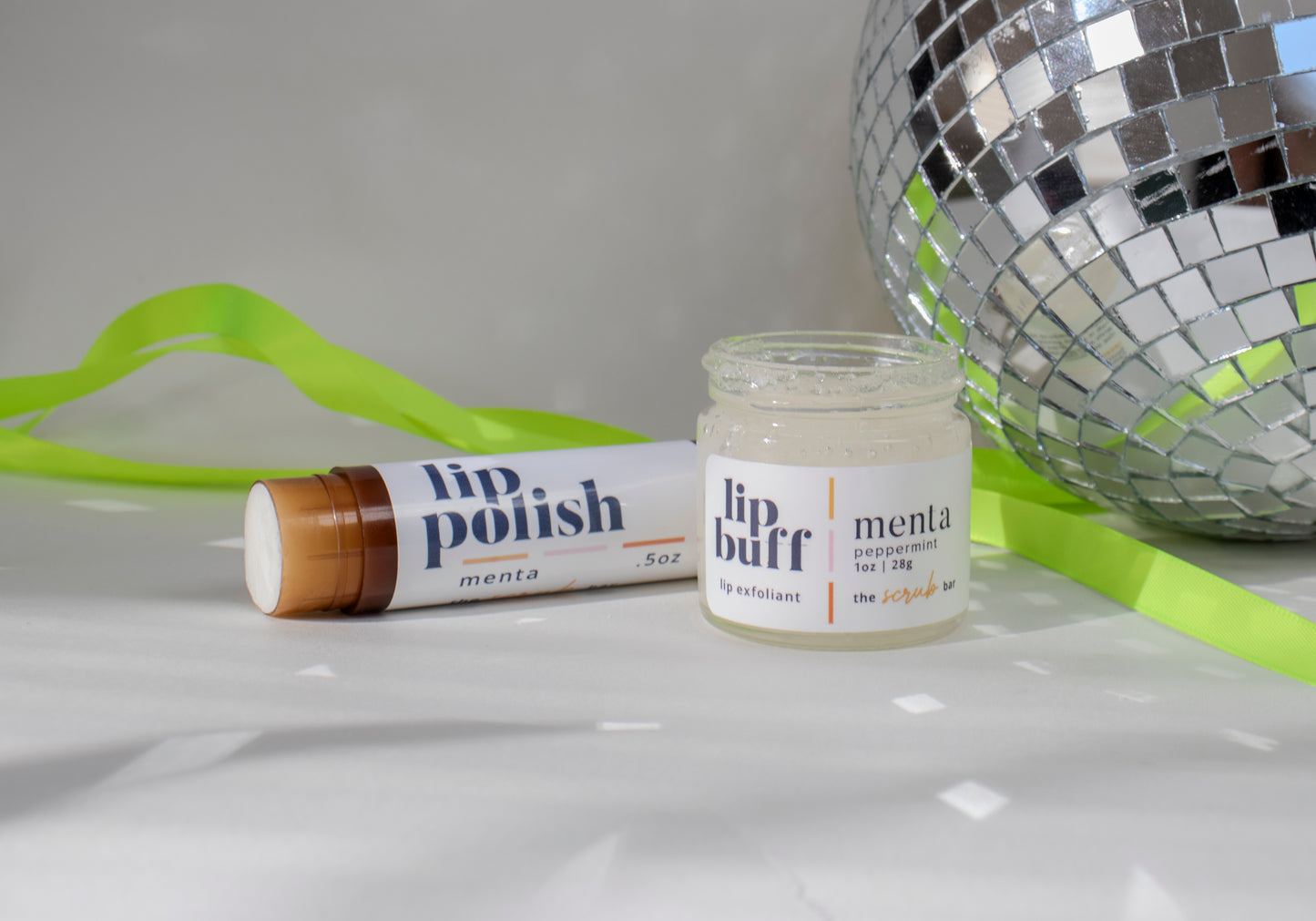 An image showcasing The Scrub Bar's peppermint exfoliating lip scrub alongside a matching lip polish stick. Both are handmade skincare products designed to exfoliate lips, revealing smooth, soft skin. Ideal for prepping lips for a polished lip oil look. 